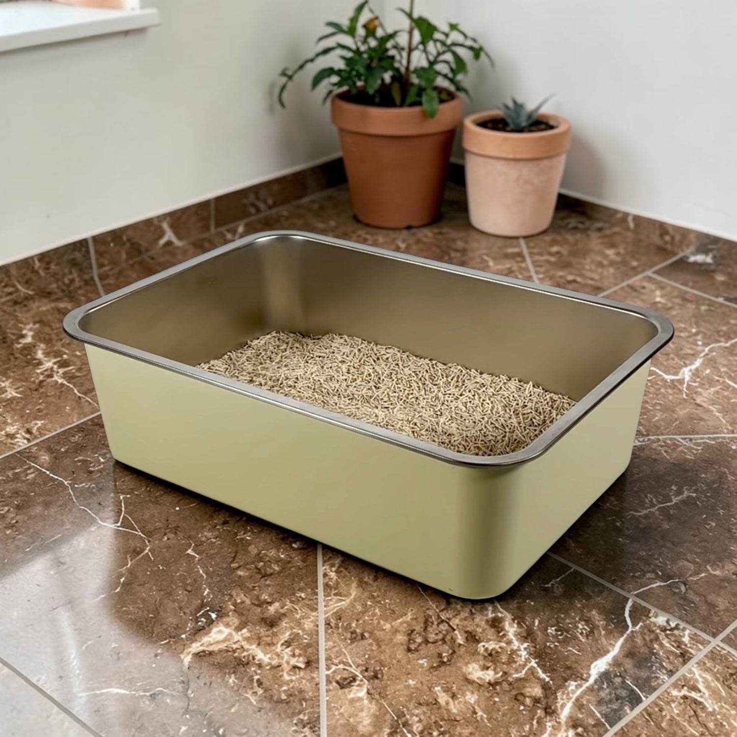 A yellow cat litter box with tofu cat litter on a tiled floor, with potted plants in the background.